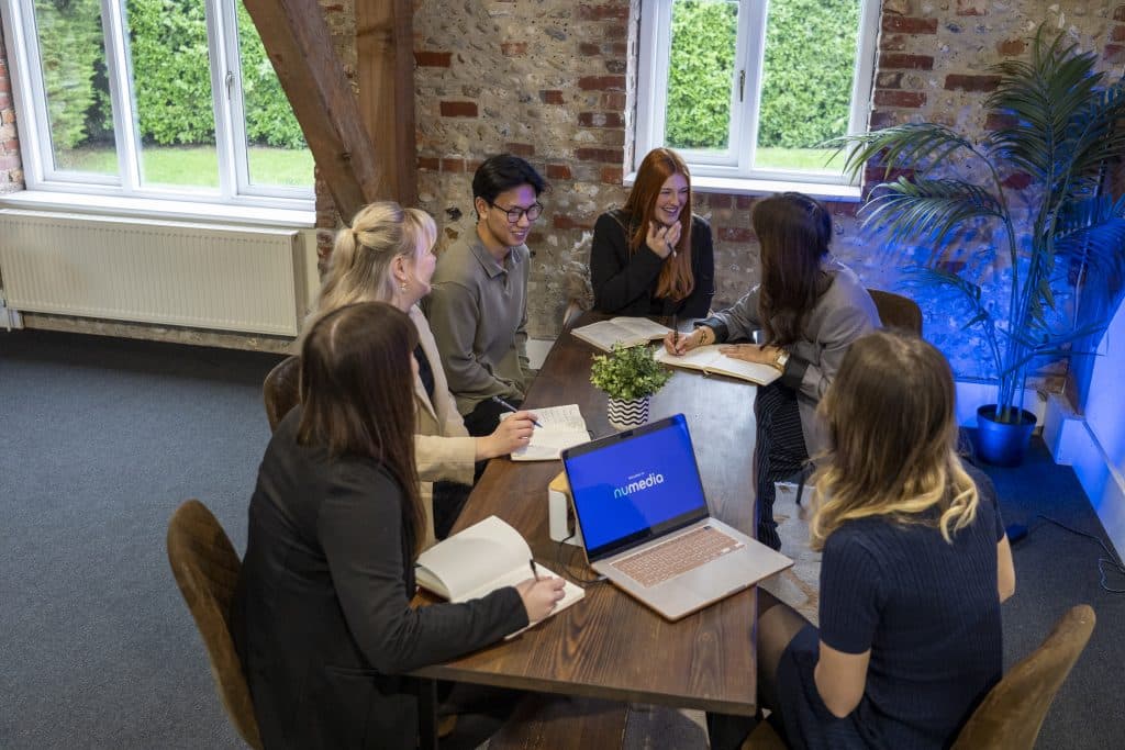 nu media group team gathered around a table with laptops and notebooks in their Bosham studio discussing Google Business Profile strategy
